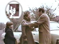 A boy watches his dad comfort his angry mum outside by the family car whilst his nan and baby sister look on from the window